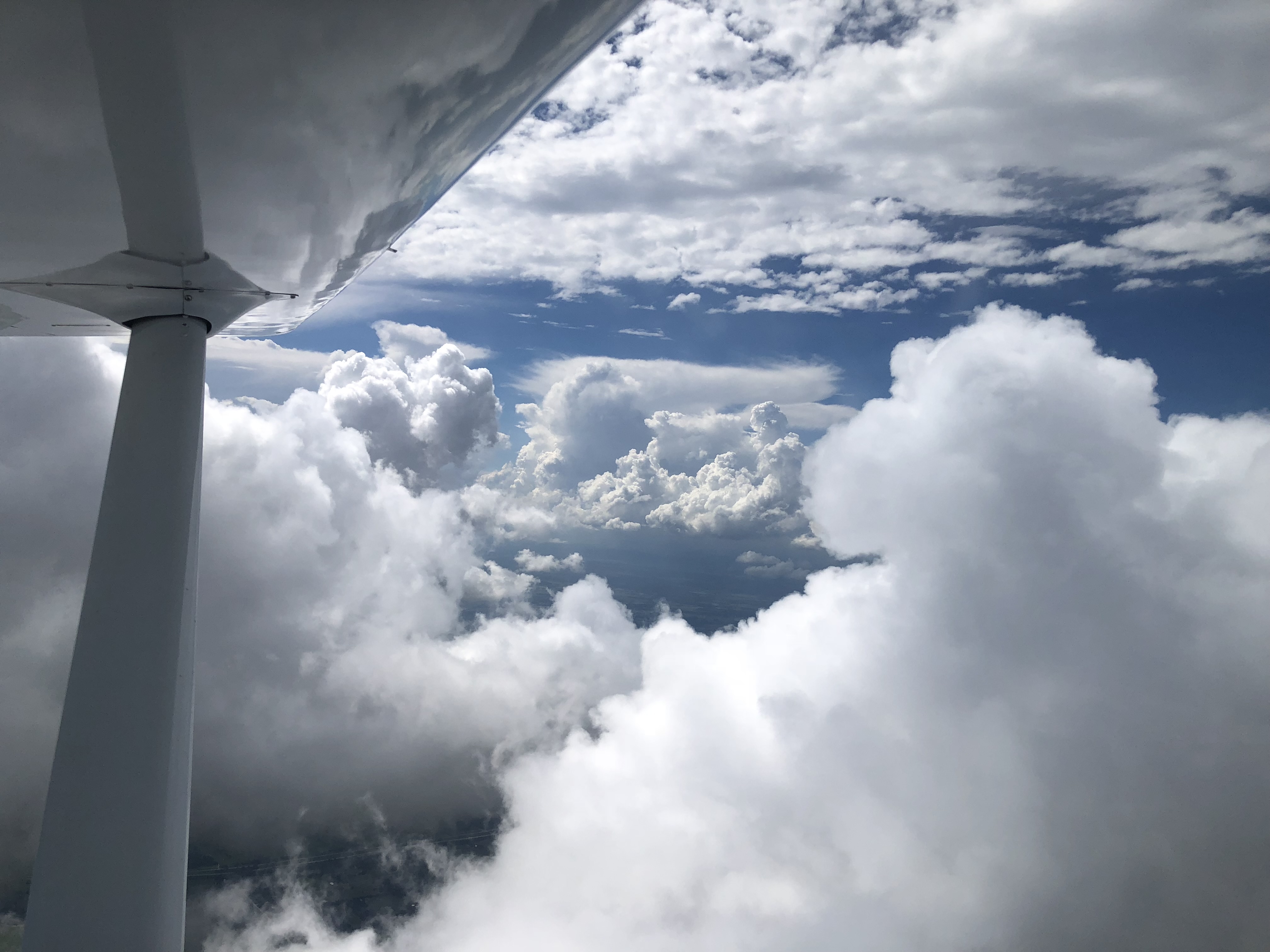 Clouds and blue sky viewed from beneath an aircraft wing.