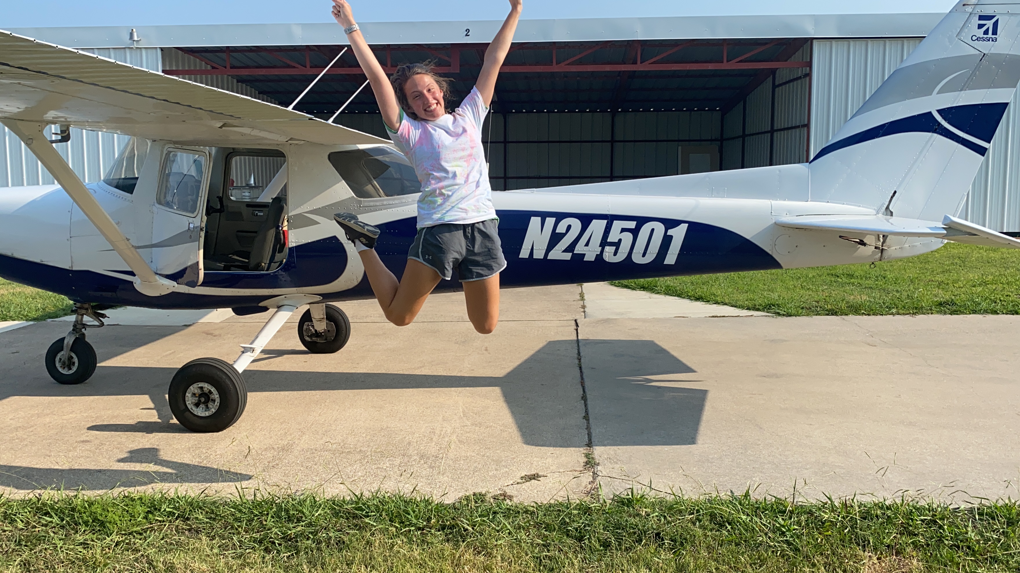A person celebrating beside a blue and white training aircraft.