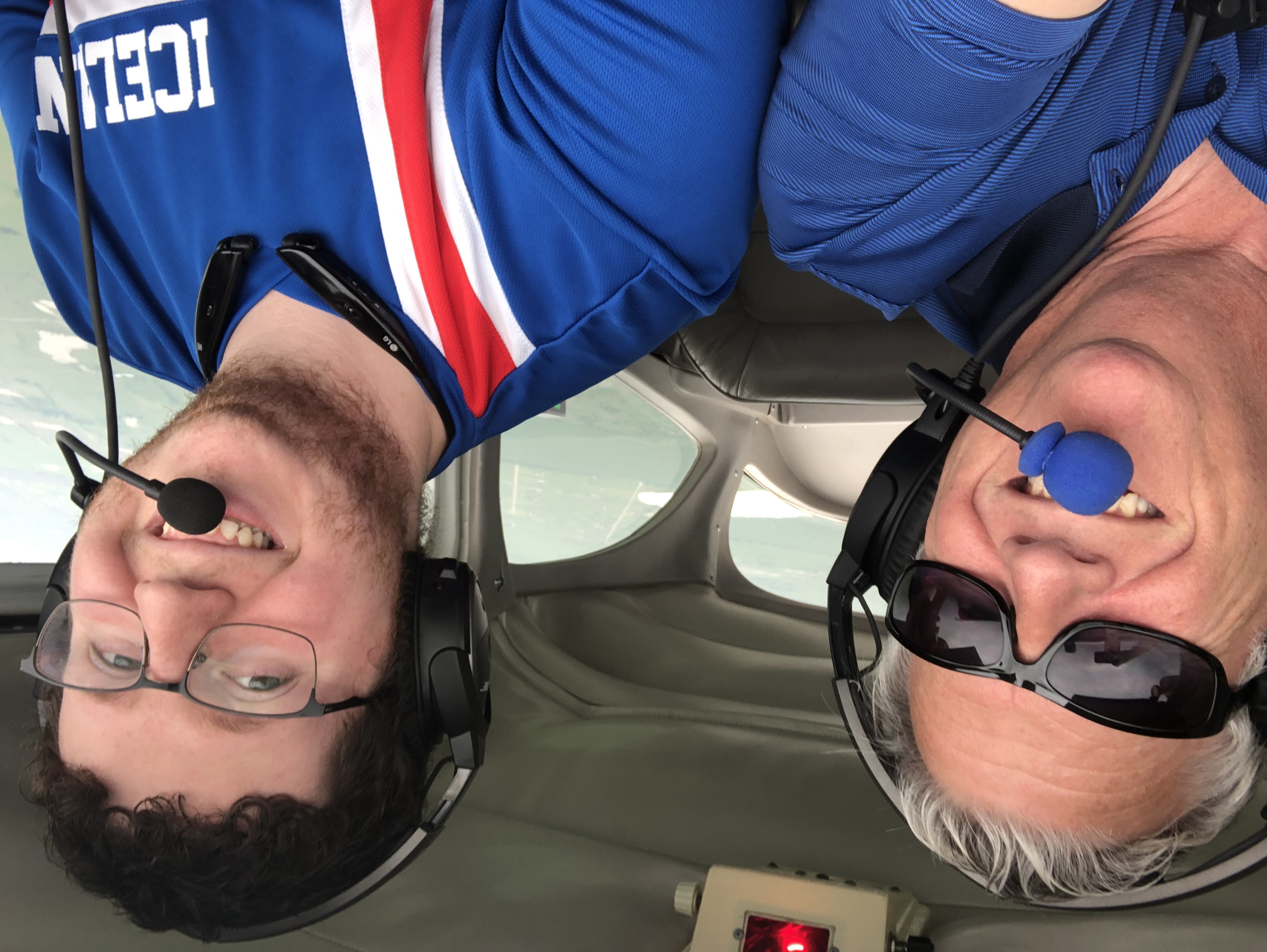 Two smiling people wearing headsets inside a light aircraft.