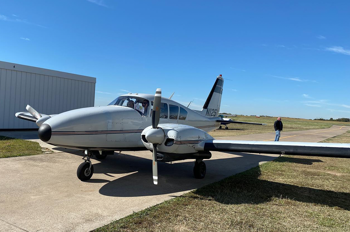 Aztec front three-quarter view outside a hangar under a blue sky.